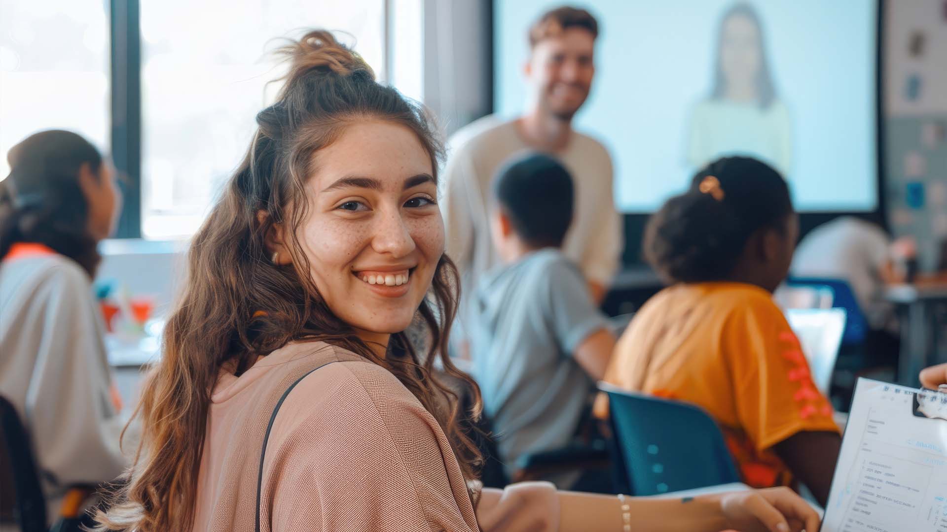 Ung kvinde smiler mens hun sidder i klasselokalet. FOTO: AdobeStock